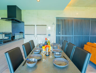 Modern dining area at Bayside Villa Miyako Island with sleek kitchen, wooden dining table set for eight, wine service, and contemporary design.