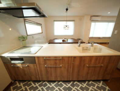 Modern kitchen island at Canal Villa Otaru with white countertops, wooden cabinetry, induction cooktop, and geometric patterned rug.