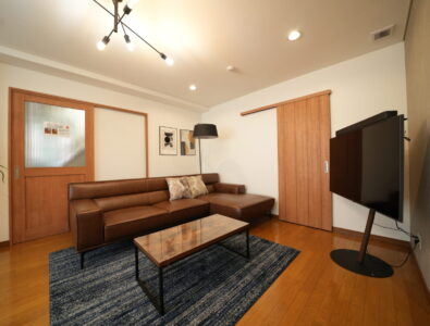 Modern living room at Canal Villa Otaru with brown leather sectional sofa, glass coffee table, flat screen TV, and warm wood accents throughout.