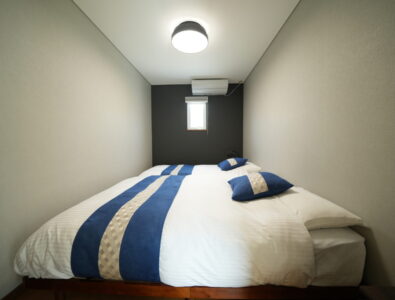 Cozy master bedroom at Canal Villa Otaru featuring queen bed with blue striped bedding, dark accent wall, and modern ceiling light.