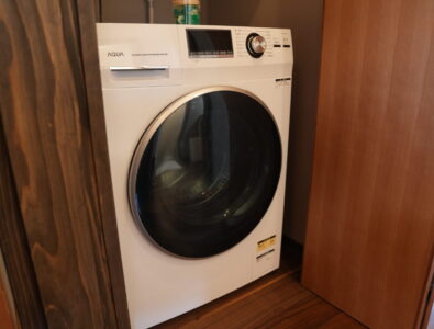 Modern AQUA washing machine at Enishiya Izumo Villa with digital display and sleek white design, built into wooden cabinetry.