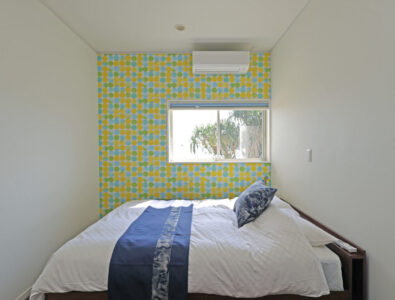 Bright bedroom at Ocean Villa Tokunoshima with colorful polka dot accent wall, queen bed, blue bedding accents, and tropical garden view.
