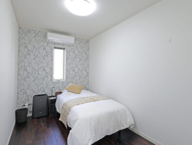 Compact single bedroom at Ocean Villa Tokunoshima with geometric accent wallpaper, white bedding, dark wood flooring, and modern amenities.