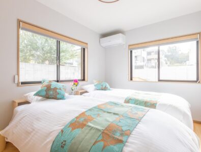 Bright twin bedroom at Ocean Villa Naruto with white bedding, turquoise floral accents, wooden frames, dual windows, and natural lighting.