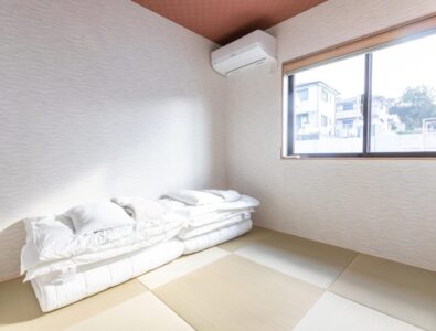 Traditional Japanese tatami bedroom at Ocean Villa Naruto with futon bedding, natural wood walls, large window, and minimalist design.